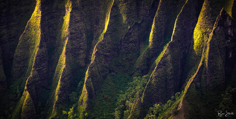 Green cliffs along the Napali Coast of Kauai are kissed by the sun as it peers in from the edge of the scene. 