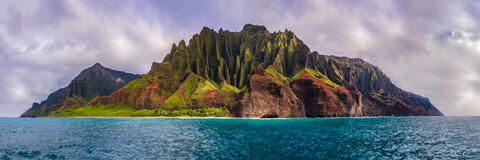 Full Napali coastline as seen from out on a boat with lush green cliffs and surrounded by turquoise blue water.
