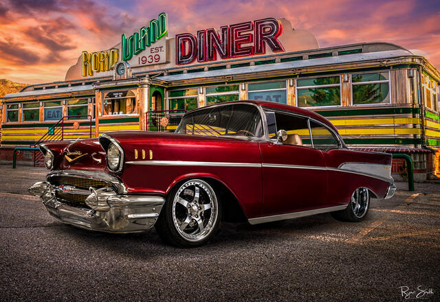 Vintage 1957 red Chevrolet Bel Air sits in front of a 1960's diner that is colored yellow and green with large neon sign lights saying "Road Island Diner".