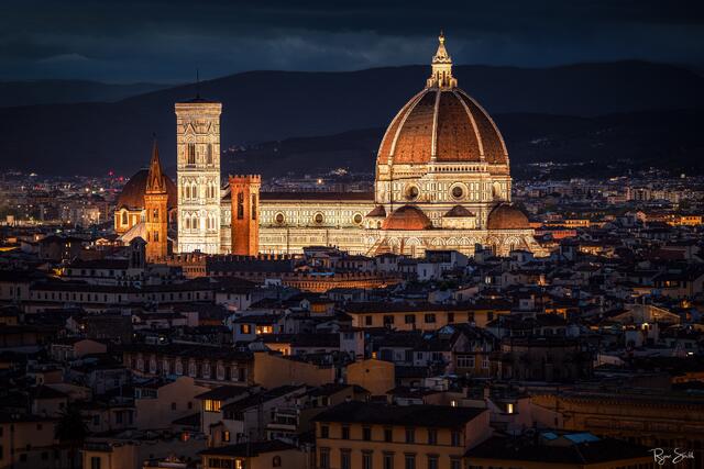 Fine art photograph of the Florence Cathedral glowing at twilight with warm architectural lighting and deep blue storm clouds, captured by Ryan Smith.