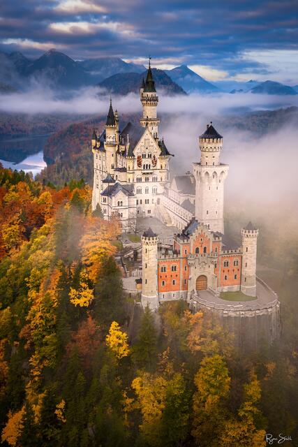 Fine art photograph of Neuschwanstein Castle in Bavaria, Germany surrounded by autumn color and morning mist, captured by Ryan Smith.