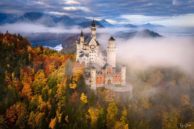 Fine art photograph of Neuschwanstein Castle in Bavaria, Germany surrounded by autumn color and morning mist, captured by Ryan Smith.