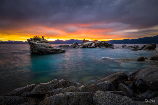 Fine art landscape photograph of Bonsai Rock at Lake Tahoe during sunset, featuring glowing skies, turquoise water, and smooth granite formations.
