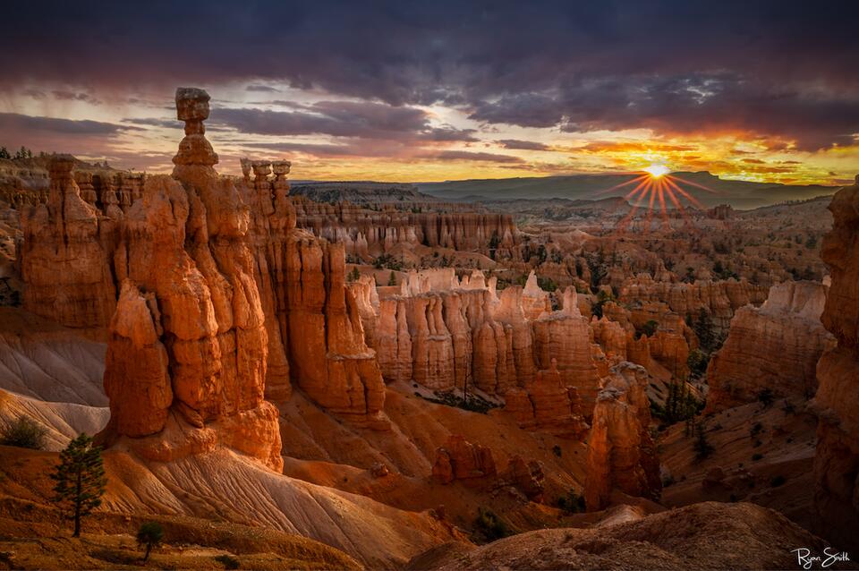 Dramatic sunrise over Bryce Canyon with fiery red, orange, and gold hues illuminating the hoodoos and rugged landscape