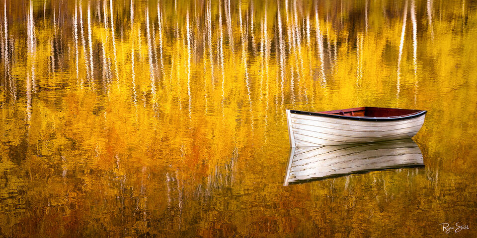 White, wooden, empty boat sits on a pond with yellow aspen trees reflecting across the water. 