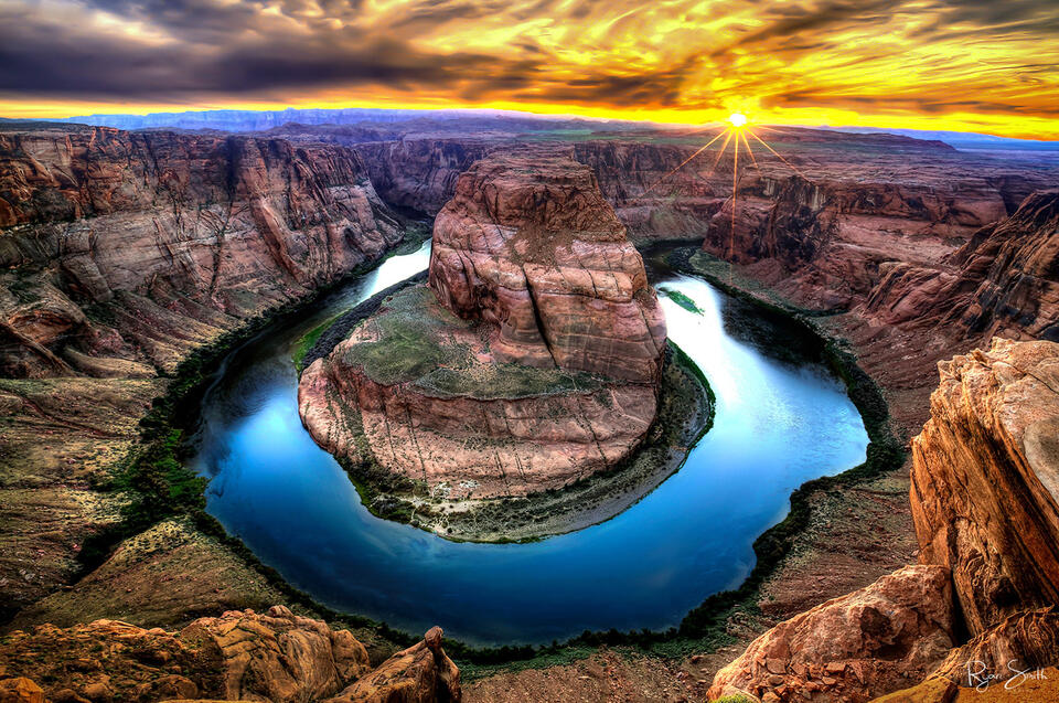 Vibrant sunrise over a large mesa and canyon view where a river bends around in the shape of a horseshoe.