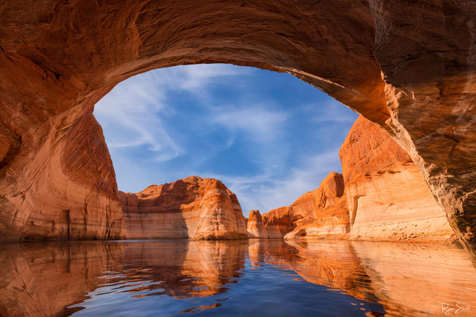A rare and unique vista of calm waters reflecting a natural arch at Lake Powell. 