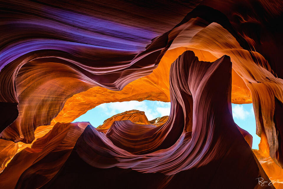 Red and taupe layers of rock swirl around with the sky barely seen through an exit in the slot canyon.