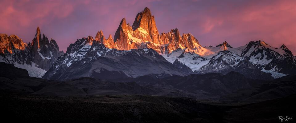 Fine art panoramic photograph of Fitz Roy in Patagonia glowing with fiery alpenglow under a magenta sunrise sky, captured by Ryan Smith.