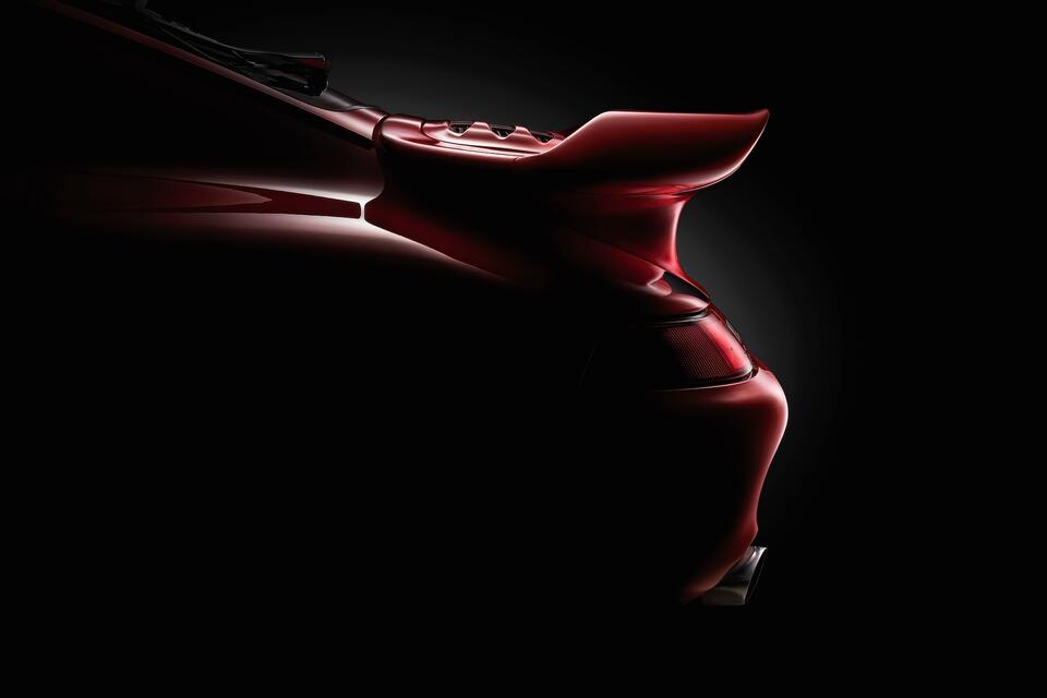 Close-up fine art photograph of the rear detail of a red 1985 Porsche 930 Turbo, with dramatic lighting emphasizing shape, curves, and reflections.