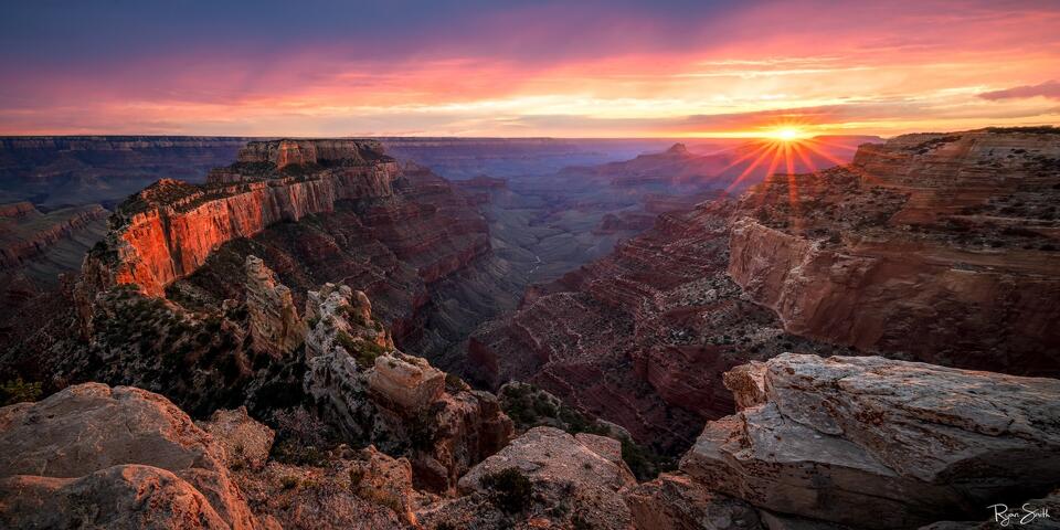 Fine art photograph of the Grand Canyon at sunset, featuring vibrant hues of orange, red, and gold illuminating the canyon's rugged landscape. A stunning repres