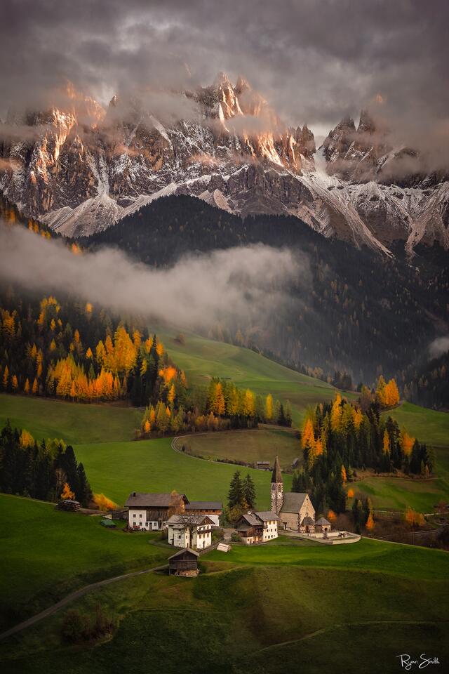 St. Magdalena at sunrise beneath glowing Dolomite peaks, drifting fog, and autumn colors—an atmospheric fine-art landscape ideal for luxury interiors.
