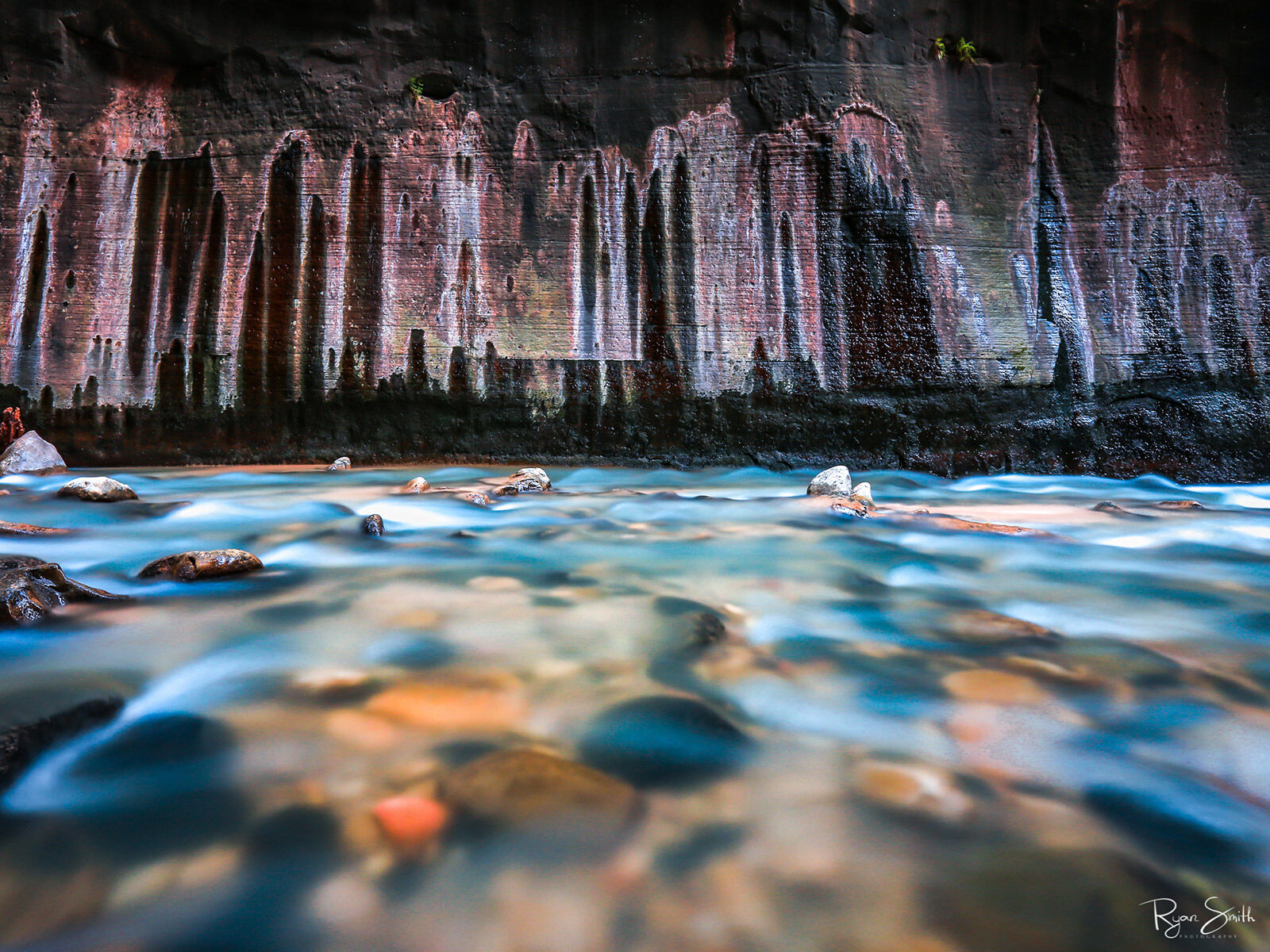 Aqua Up close photo of turquoise colored water flowing over rocks with water stains on the canyon wall appearing like a skyline.