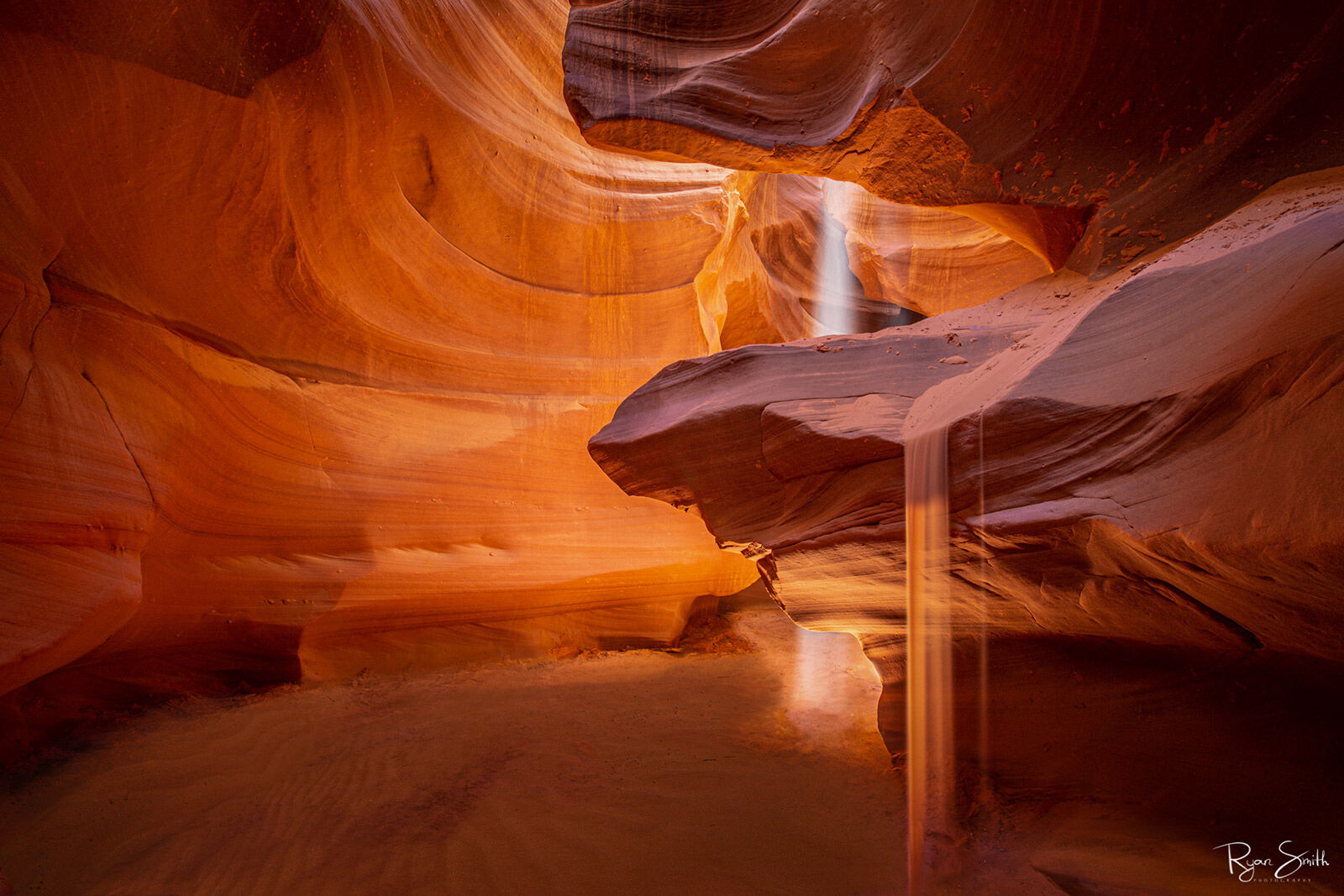 Sands of Time View from in a slot canyon where a beam of light shined in and sand falls from the sandstone shelf is filled with orange and yellow tones and no sky is seen.