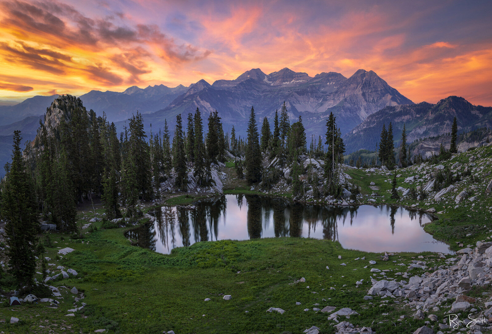 Silver Glance Mountain skyline at sunset with pink and orange clouds and spruce trees reflecting in a small lake.