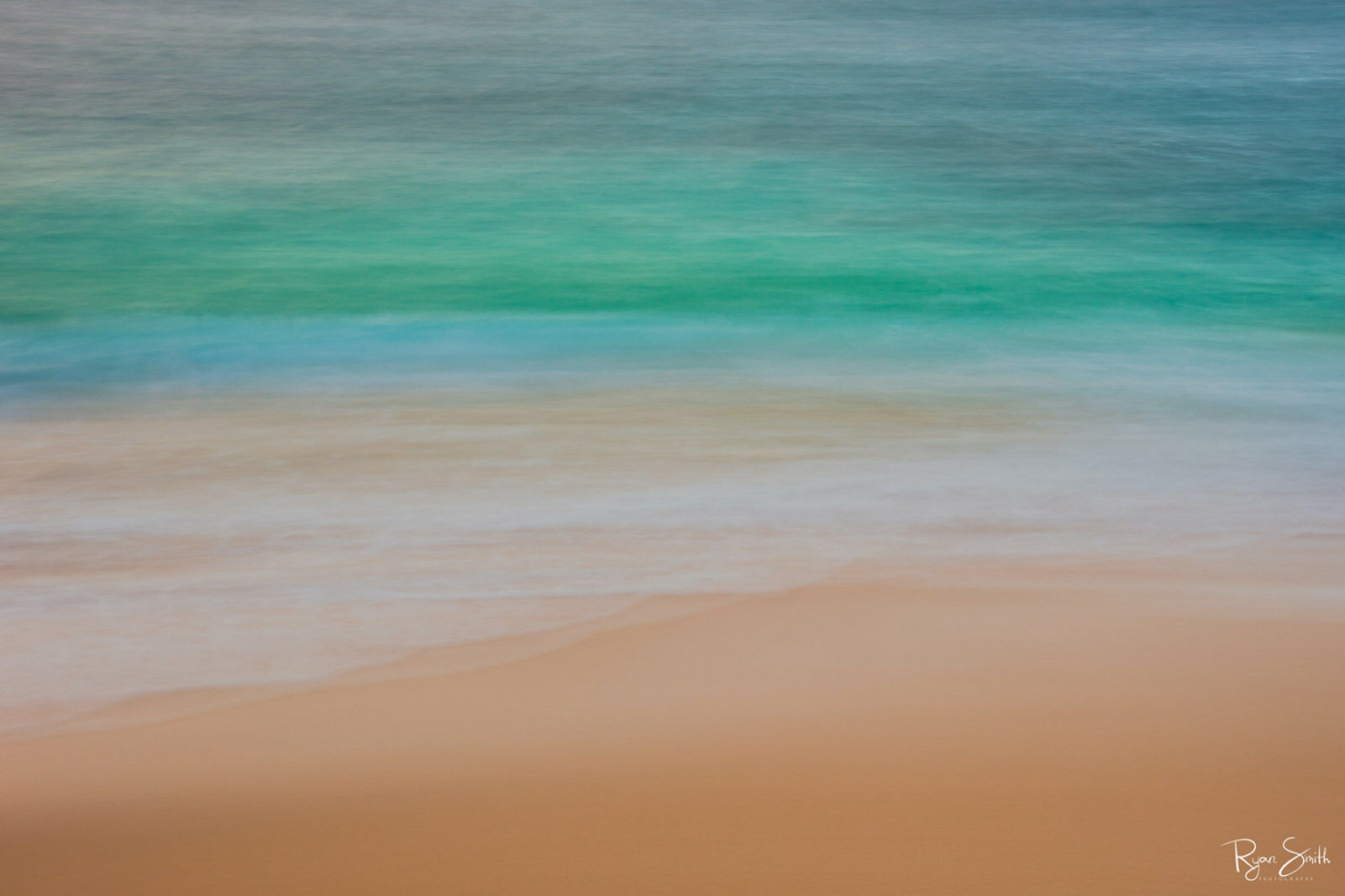 Abstract photography of the beach close up with the tan sand, shallow water and deep turquoise and blue water out further.