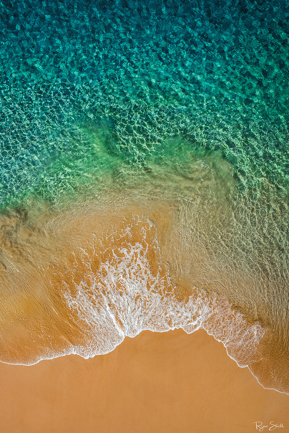 Emerald Waters Aerial view of a tropical beach with vibrant turquoise and green waters gently washing onto golden-orange sands, framed by the natural beauty of the coastline.